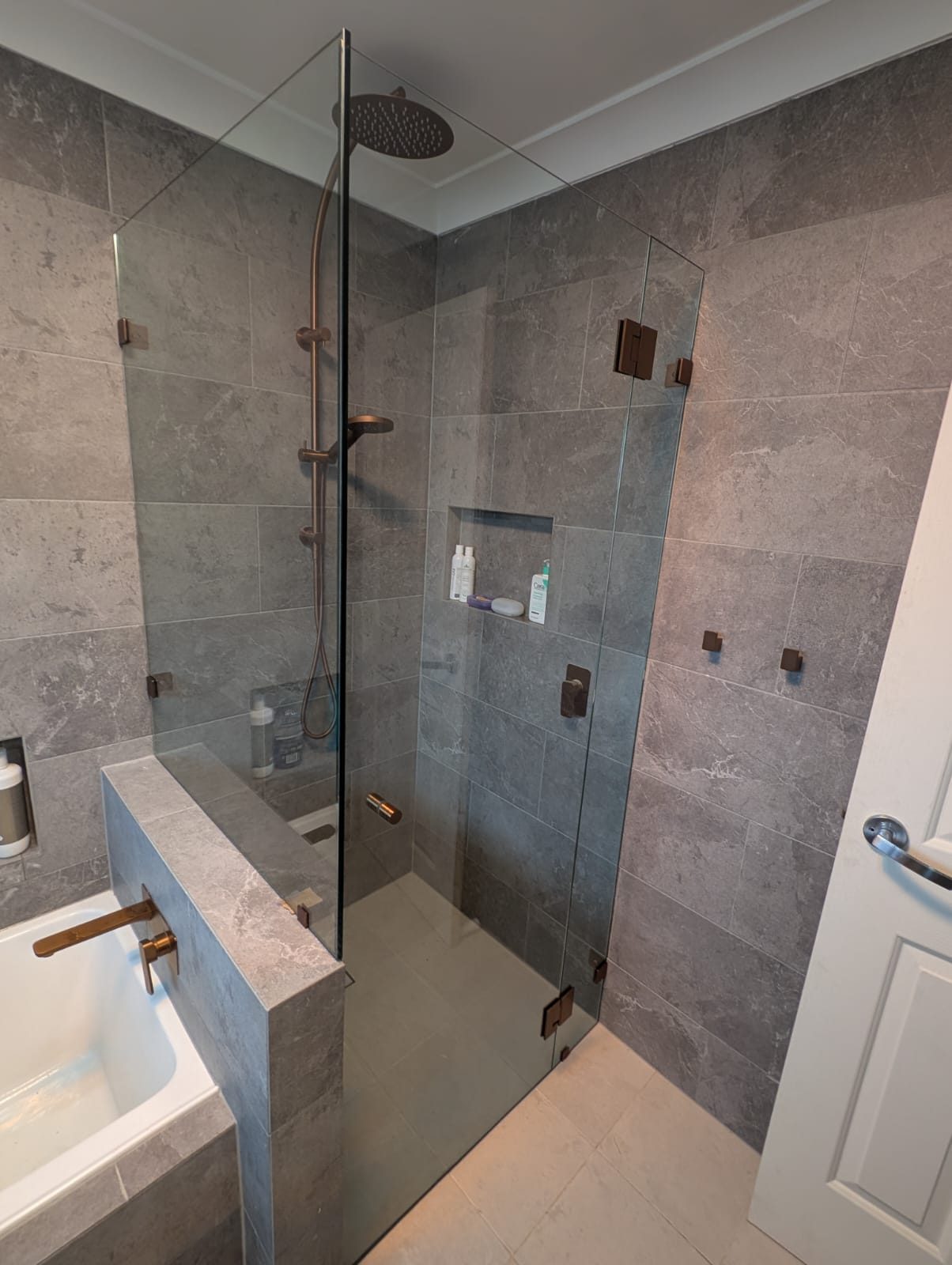 Frameless corner shower screen with copper hardware on grey tiles