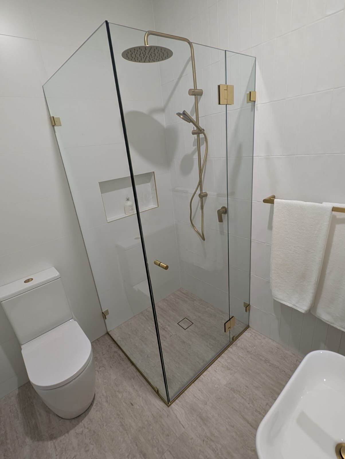 Frameless corner shower with brass fittings against white tiles