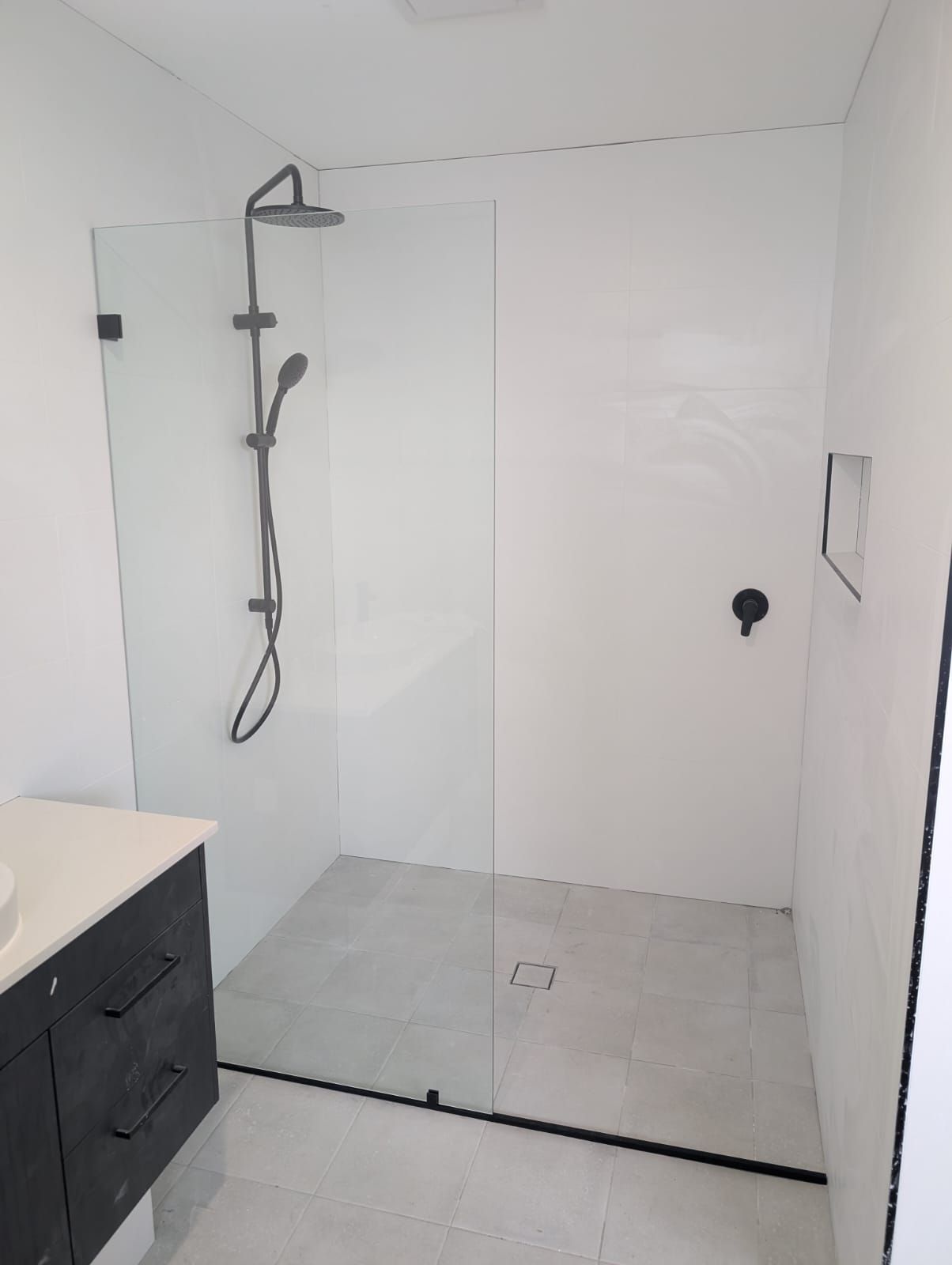 Frameless fixed shower panel with matte black bracket and floor channel