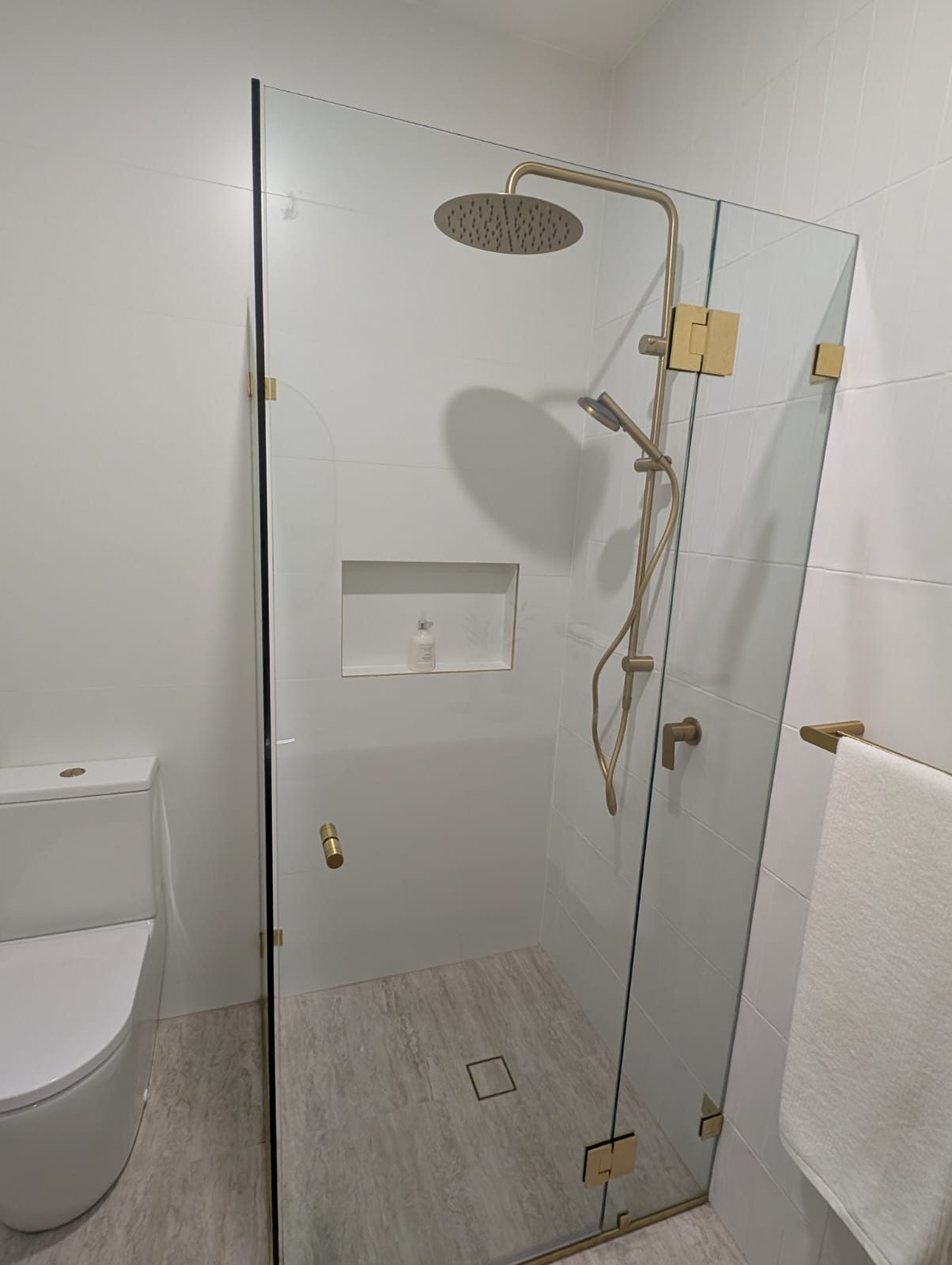 Brushed brass hinges on a frameless shower door