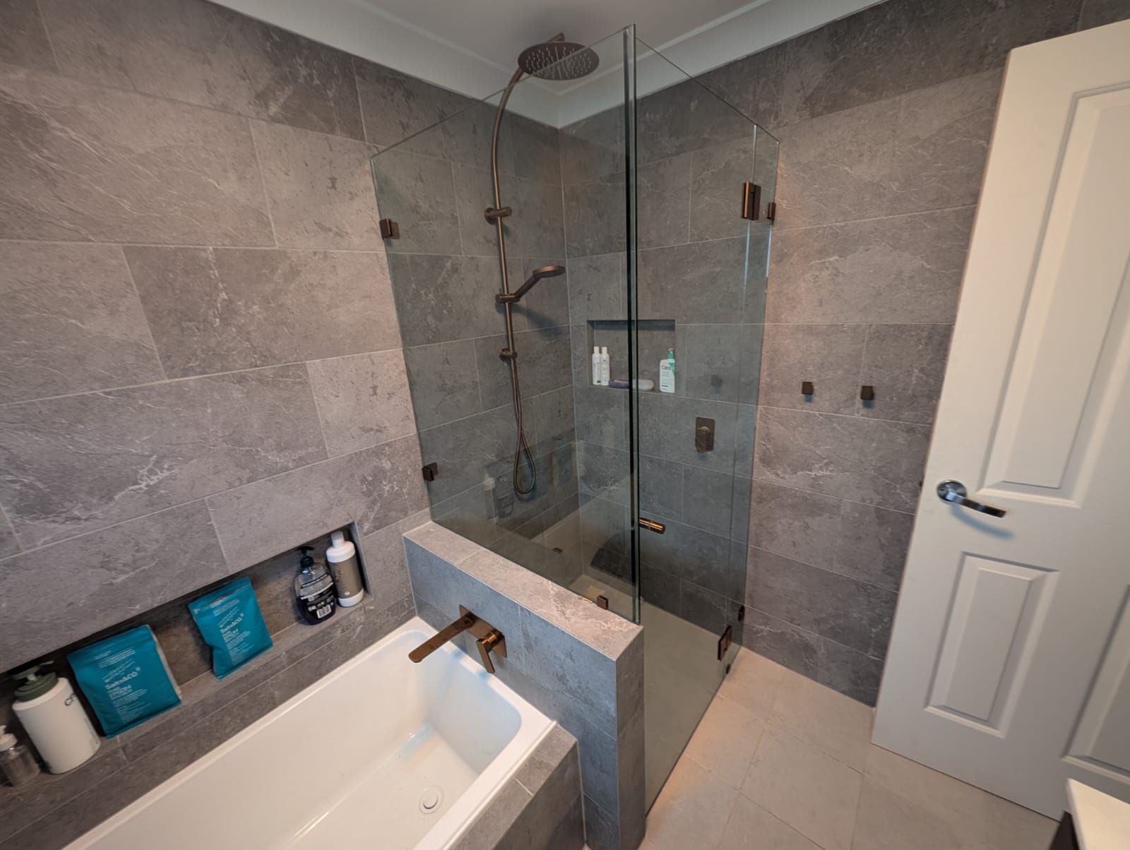 Frameless shower enclosure with copper hinges next to a built-in bath