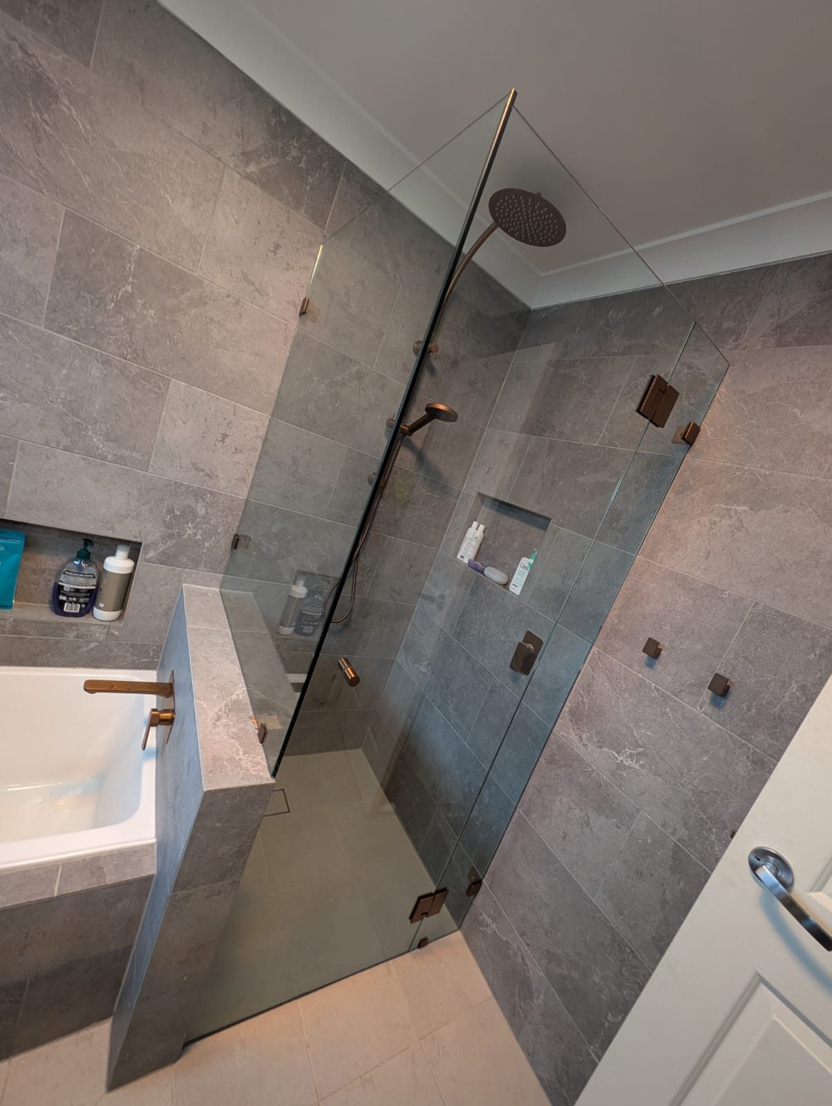 Frameless shower screen fixed to a tiled half wall with copper clamps