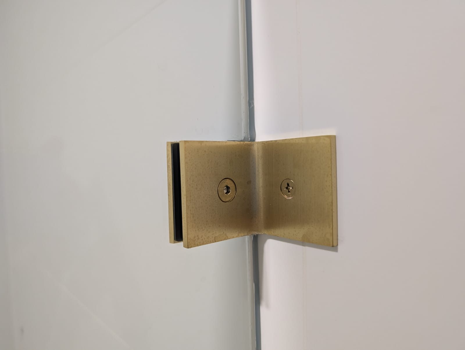 Brushed brass wall clamp holding a frameless glass panel